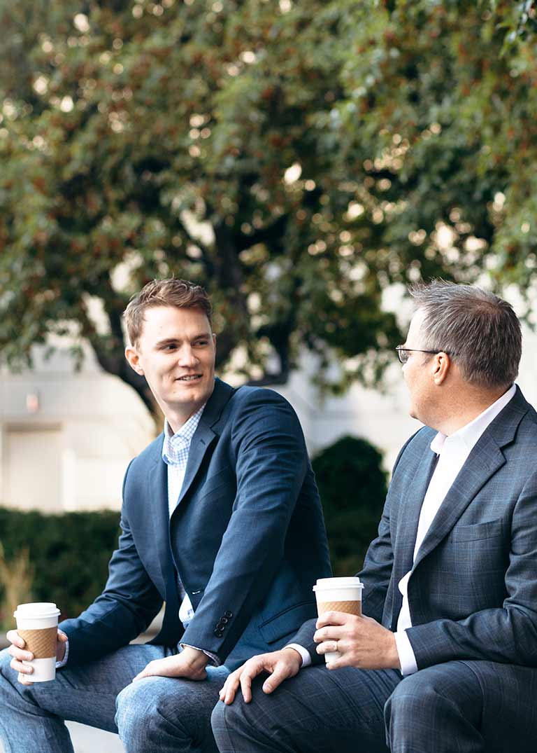 Two men talking to each other outside and holding coffee cups