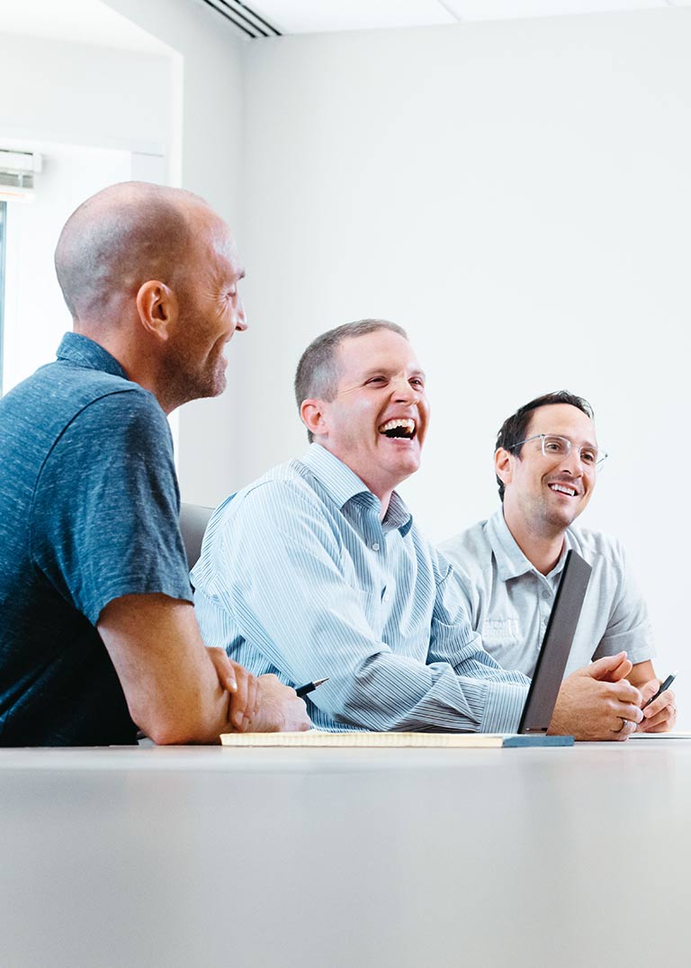 Image of three men sitting at a table and laughing together.