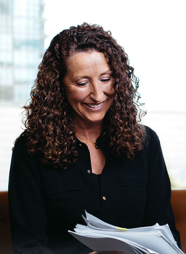 Curly haired woman smiling at a stack of papers in her hands.